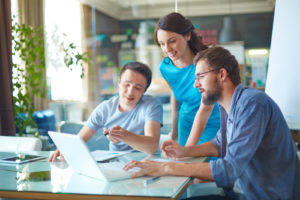 Group of three successful business partners in casual discussing data in laptop at meeting in office
